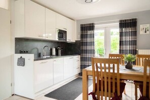 Eine moderne Küche mit weißen Schränken, einer schwarzen Arbeitsplatte und einem Essbereich mit Holztischen und einem Tisch.