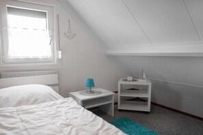 Een slaapkamer met een bed, nachtkastje, lamp, plank en een raam.