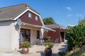 Ein zweistöckiges Haus mit geneigtem Dach, einer Satellitenschüssel und einer Terrasse mit Gartenmöbeln.