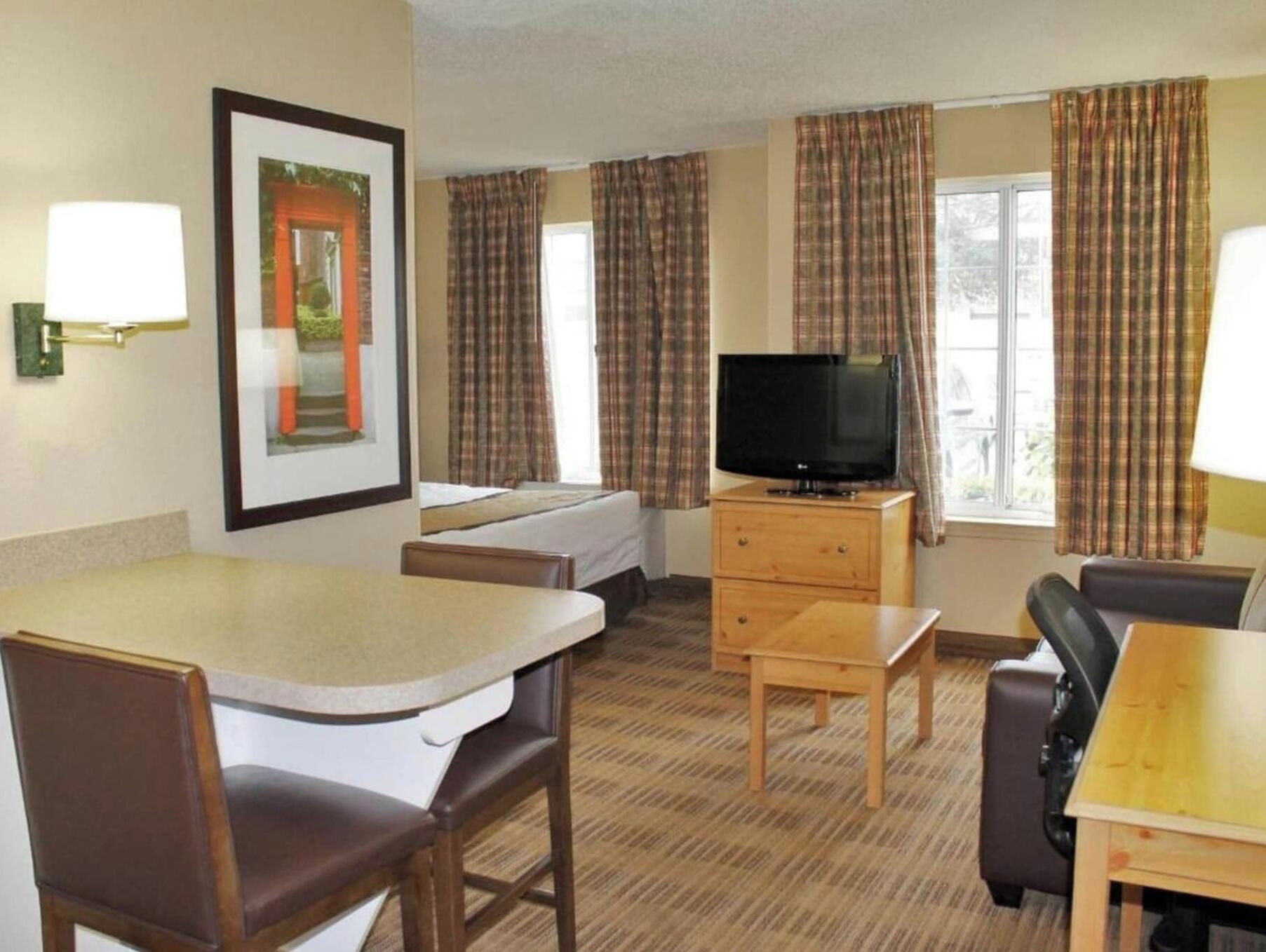 A hotel room with a bed, a television on a wooden stand, a desk, and a chair.