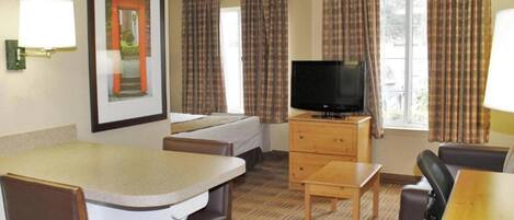 A hotel room with a bed, a television on a wooden stand, a desk, and a chair.