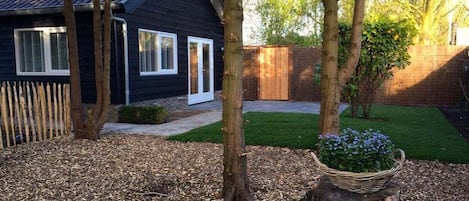 A residential property with a dark-colored house, a wooden fence, a lawn, and a tree stump with a basket of flowers.