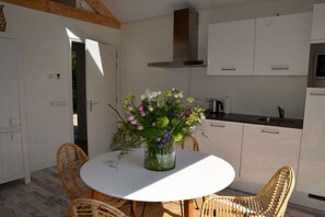 Eine moderne Küche mit weißen Schränken, einer Edelstahl-Dunstabzugshaube und einem Essbereich mit Korbstühlen und einem weißen Tisch.