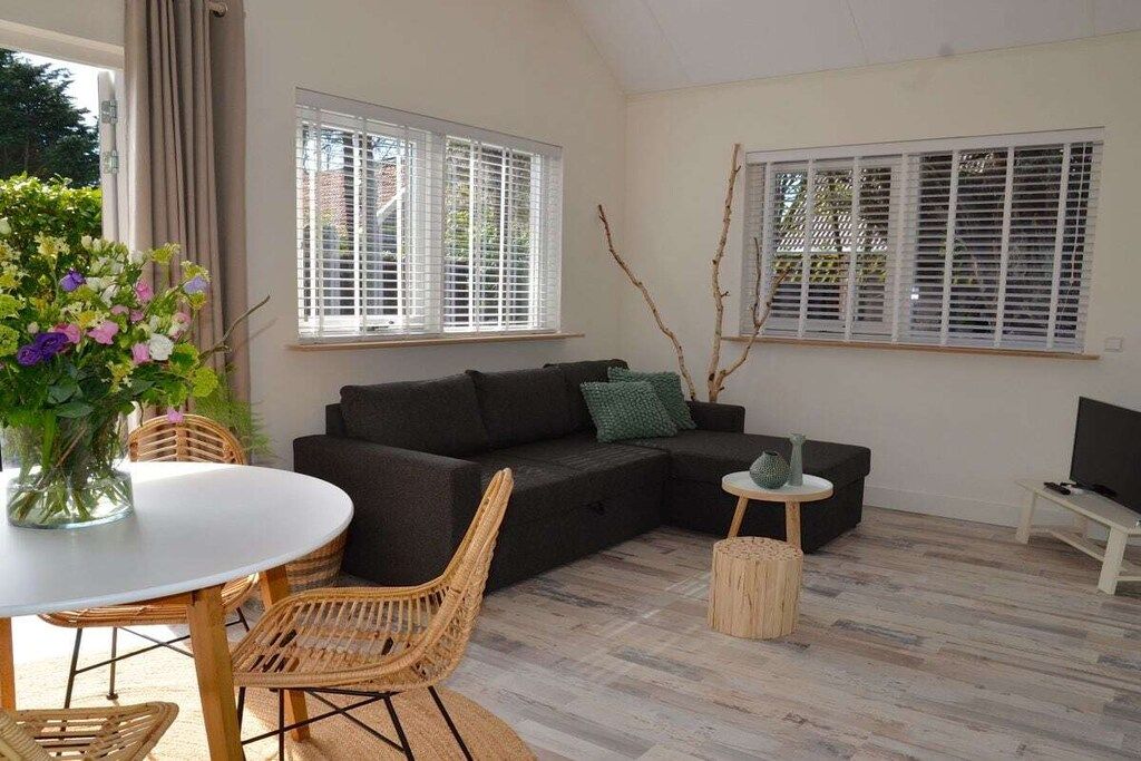 Een moderne woonkamer met een hoekbank, een ronde eettafel, rieten stoelen, een klein bijzettafeltje en een televisie.