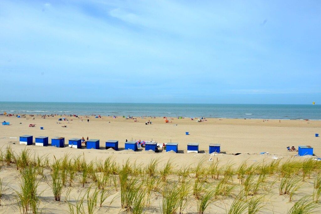 Une plage avec des cabanes de plage bleues et des personnes visibles au loin.