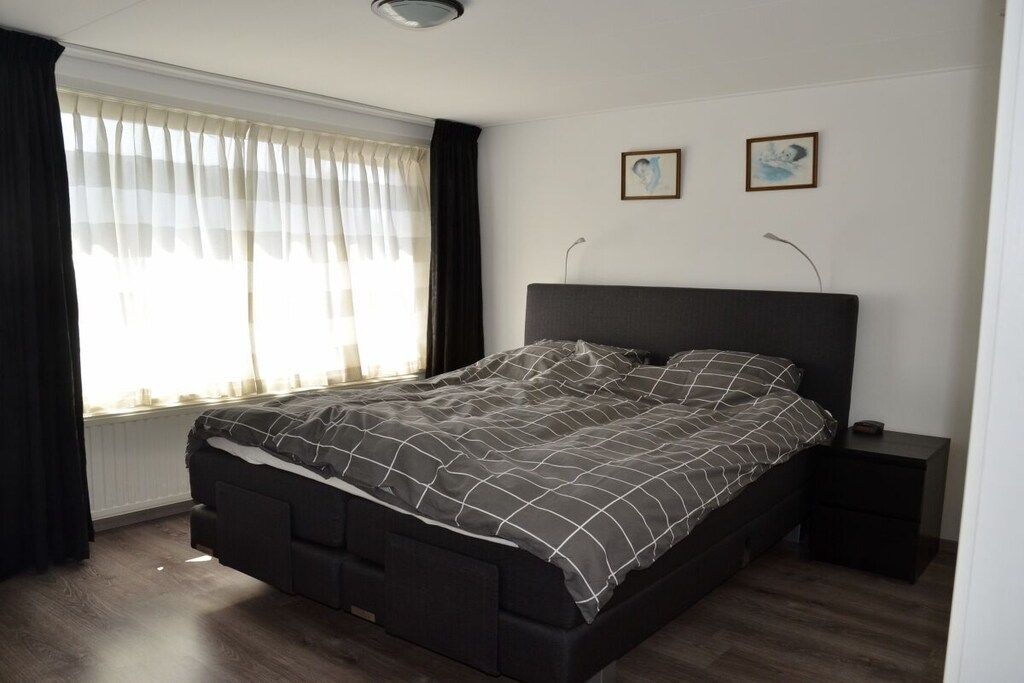 A bedroom with a bed, bedside tables, a window with curtains, and two wall-mounted pictures.