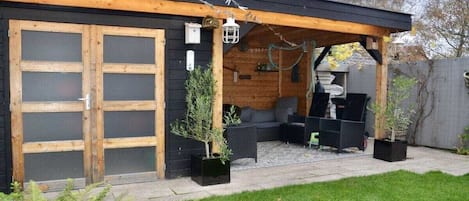 Ein Holzhaus mit überdachter Terrasse, einer Schiebetür und Sitzgelegenheiten im Freien.