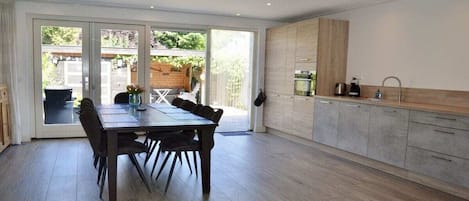 A modern kitchen with a dining area, large windows, and a view of the outdoors.
