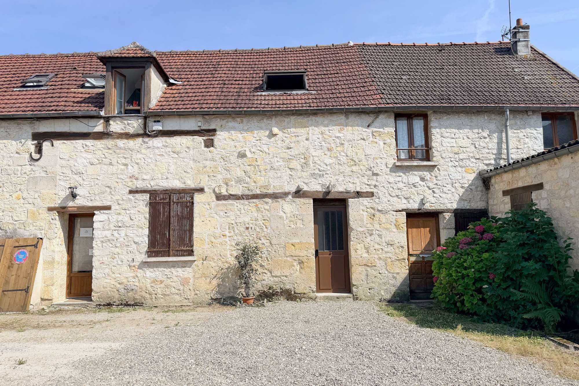 Edifici de pedra amb teulada a falda, dues portes de fusta i un camí d'accés de grava.