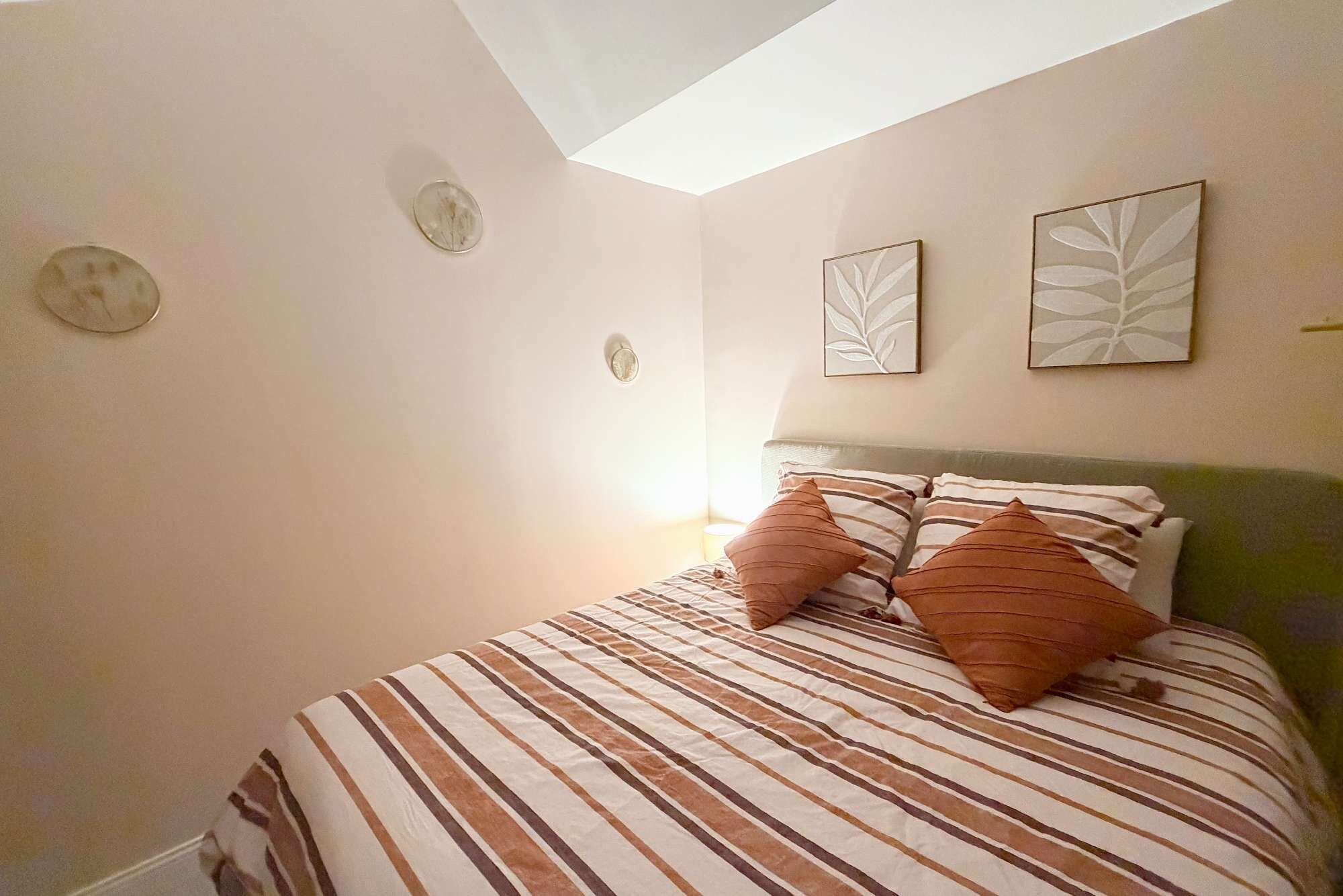 Un dormitorio con cama, dos almohadas, una mesita de noche y decoración en la pared.