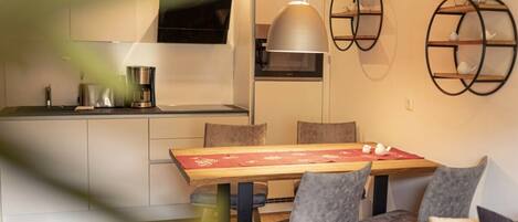 A modern kitchen with a dining area, featuring a wooden table, grey upholstered chairs, and a pendant light.