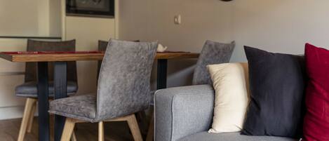 Una sala de estar moderna con un sofá gris, una mesa de centro de madera y sillas grises. Hay una zona de comedor con una mesa y sillas de madera.