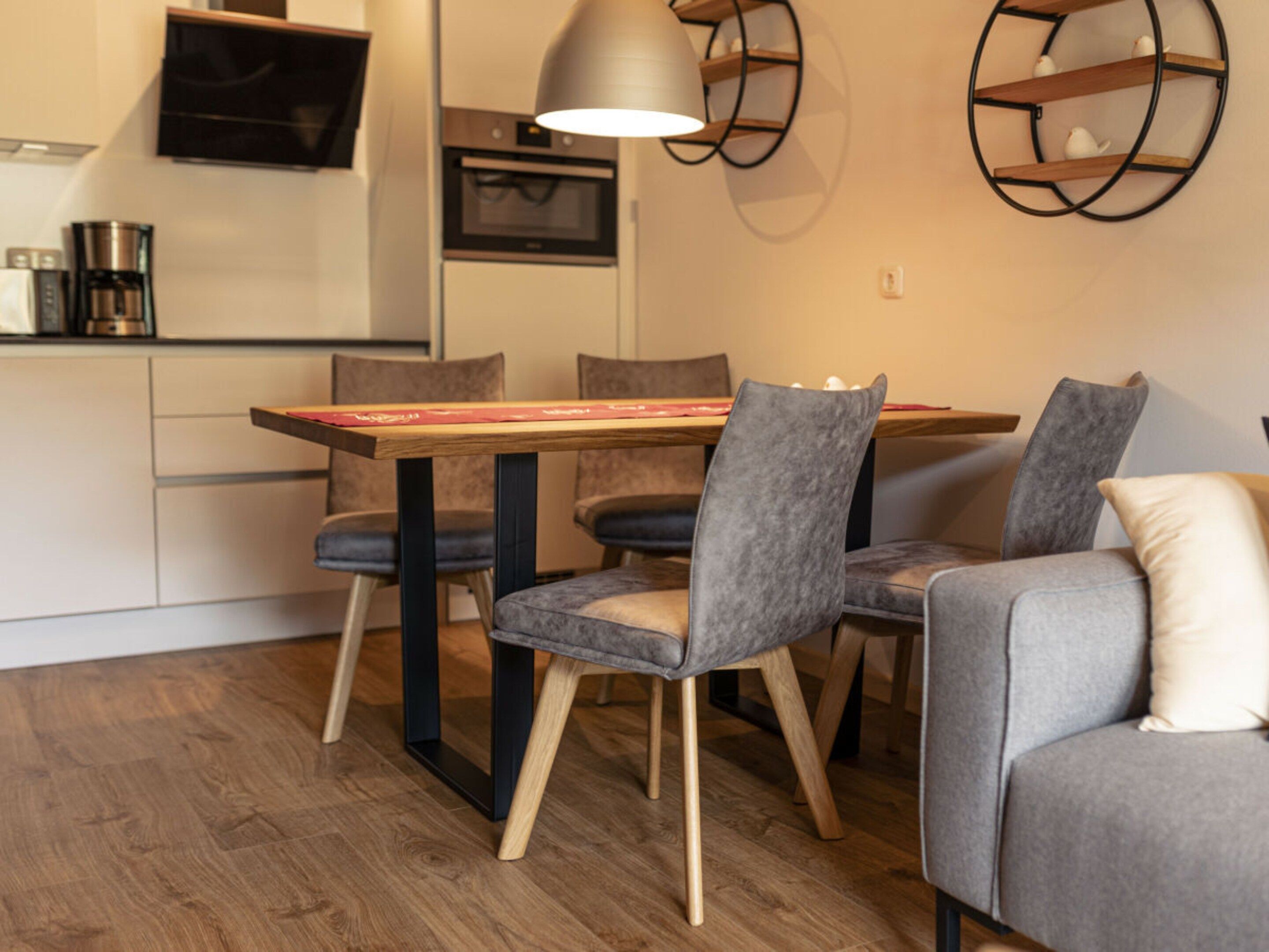 Cocina moderna con comedor, que incluye una mesa de madera, sillas tapizadas en gris y una lámpara colgante.