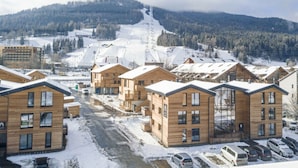 En snötäckt by med trähus, en skidbacke i bakgrunden och en klar himmel.