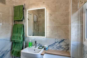 A bathroom with a white sink, a mirror with a light, a green towel, and a shower.