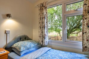Ein Schlafzimmer mit einem Bett, einem Nachttisch, einer Lampe und einem Fenster mit Vorhängen.