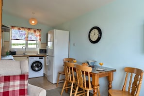 A compact kitchen with a washing machine, a refrigerator, and a dining area with wooden chairs and a table.