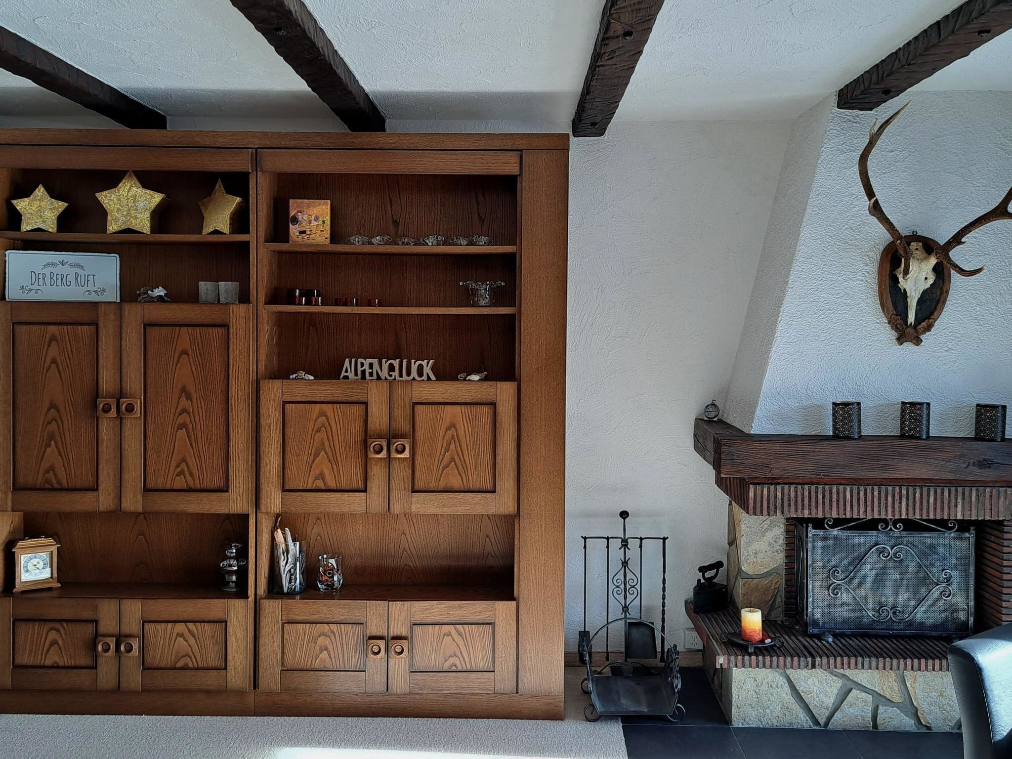 Een houten kast met meerdere vakken, een open haard met een stenen omlijsting, en een opgehangen herten schedel aan de muur.