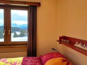 A bedroom with a bed, a window with curtains, and a wall-mounted shelf with decorative items. - Stgirat Bellaval Appartement/Fewo,   2.5 ZiWgh. Stgirat Bellaval by Interhome (Valbella)