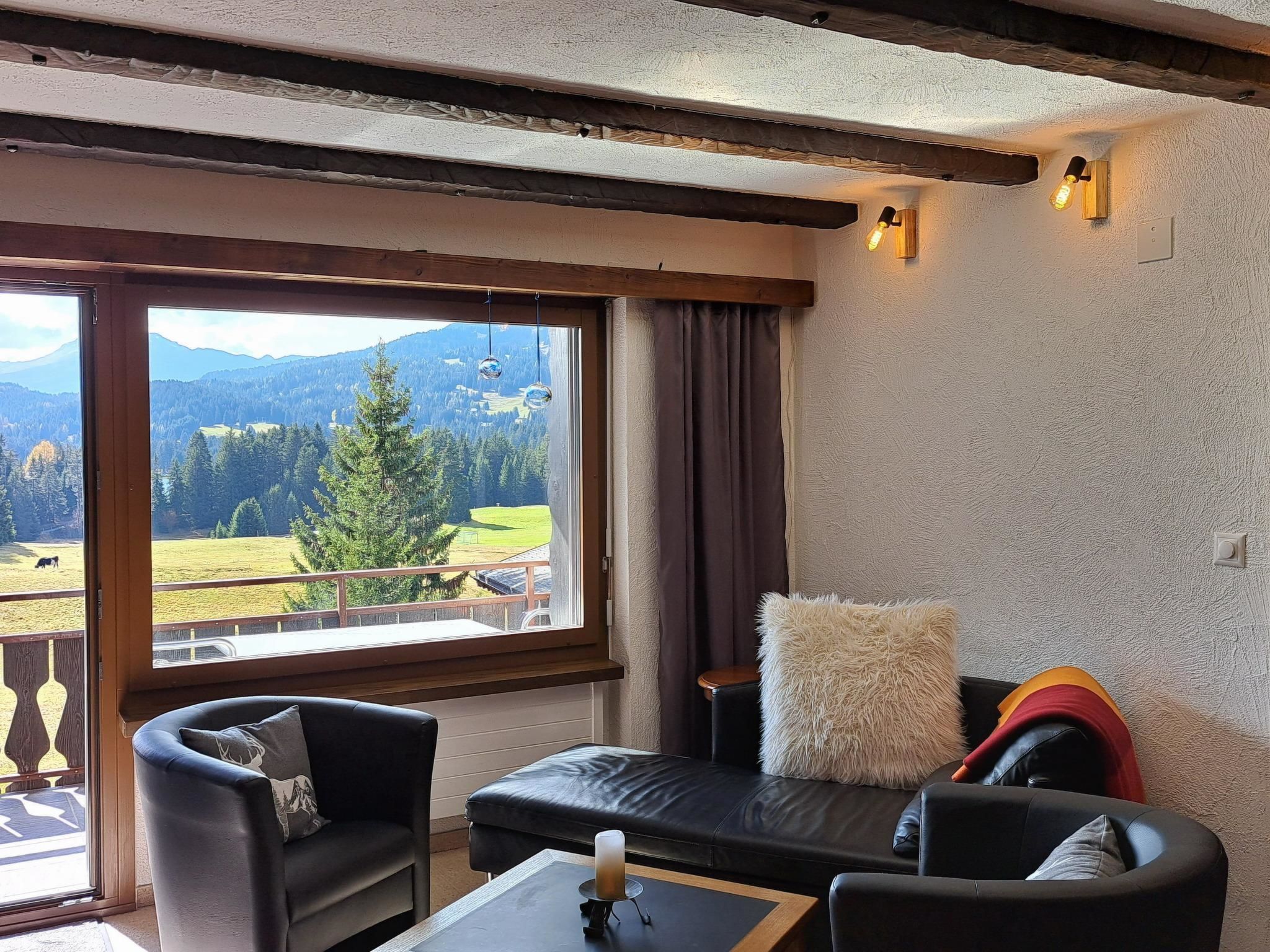 Une pièce avec vue sur un paysage montagneux, comprenant un canapé, un fauteuil et une table sur laquelle est posée une bougie.