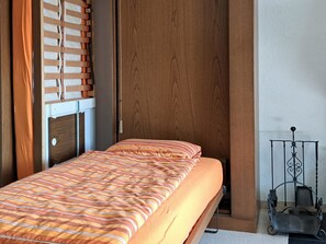 Ein Einzelbett mit gestreifter Bettdecke in einem Zimmer mit Holzwänden und einem Metallgestell.