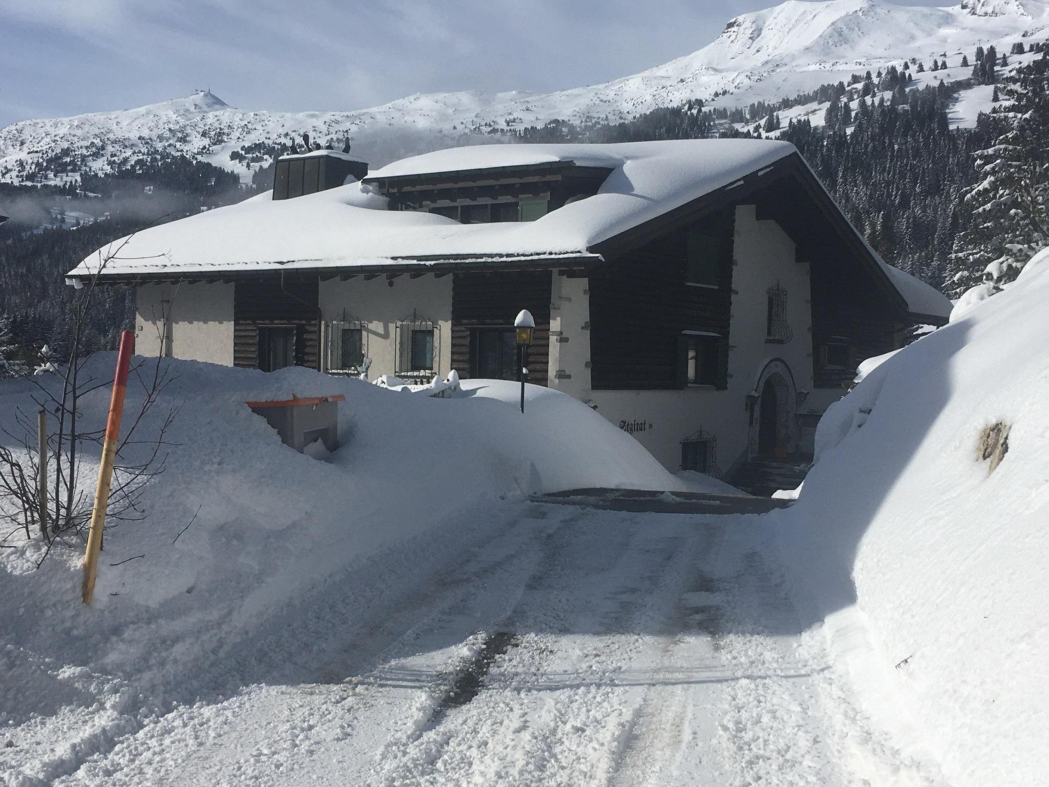 Eine schneebedeckte Lodge mit geneigtem Dach, einer kleinen Veranda und einem sichtbaren Schornstein.