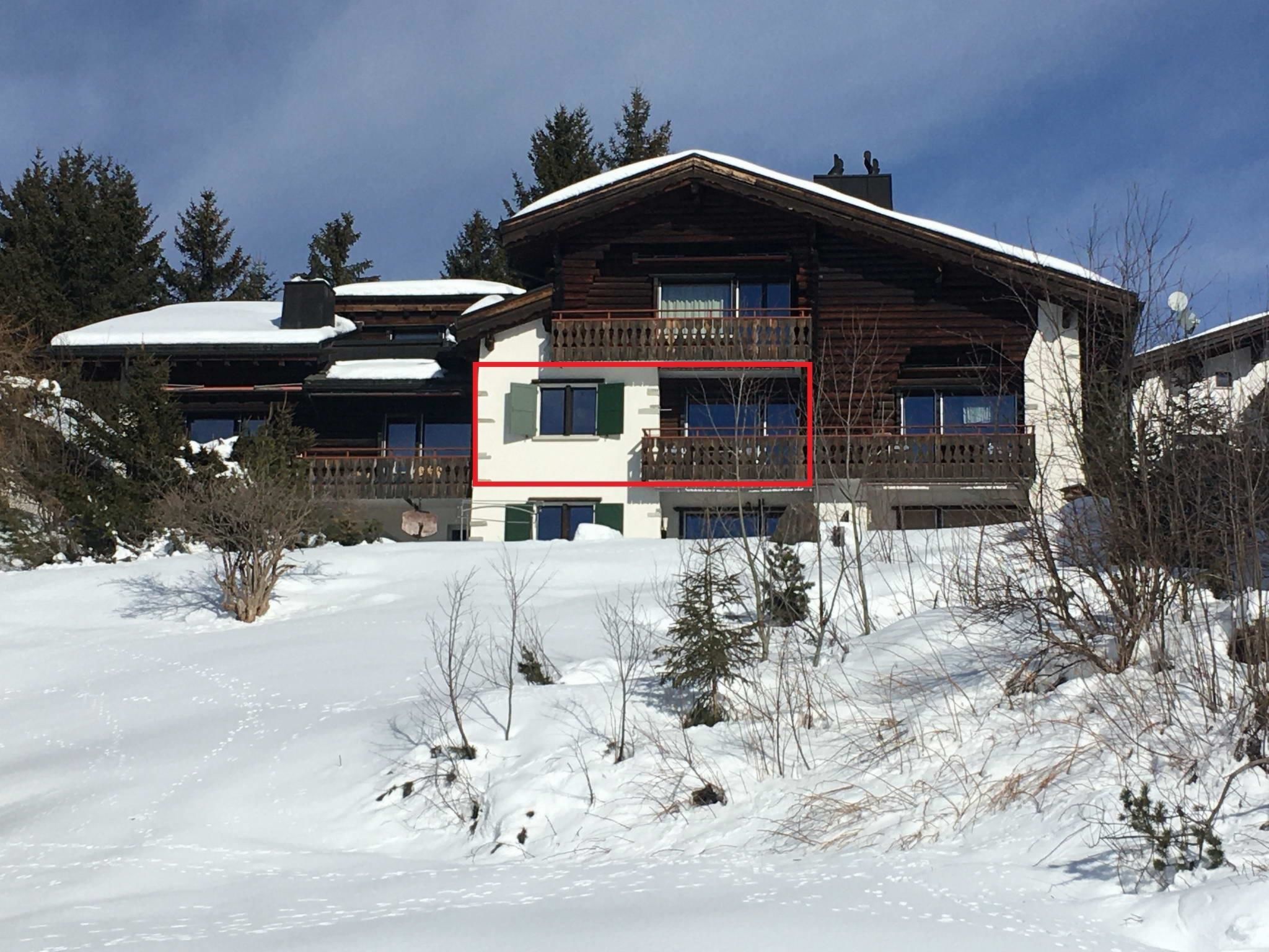 Un bâtiment en bois à plusieurs étages, doté d’un balcon, entouré d’un paysage enneigé et d’arbres.