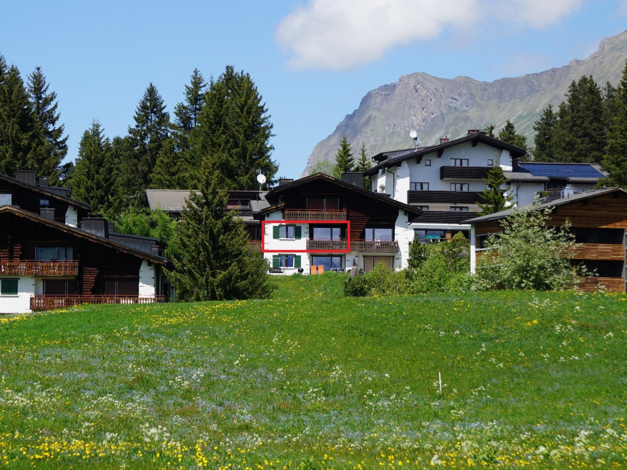 Een bergresort met meerdere chalets, een weide vol bloemen en een berg op de achtergrond.