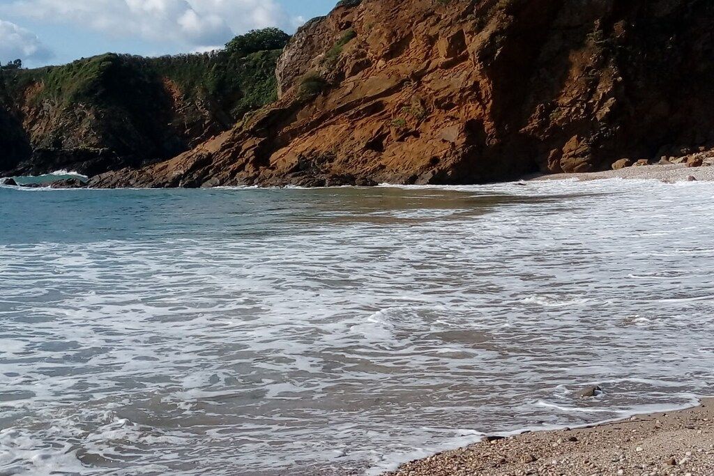 A coastal beach with waves, rocky cliffs, and a pebbly shore.