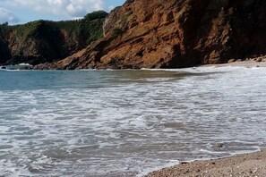Ein Küstenstrand mit Wellen, felsigen Klippen und einem Kiesufer.