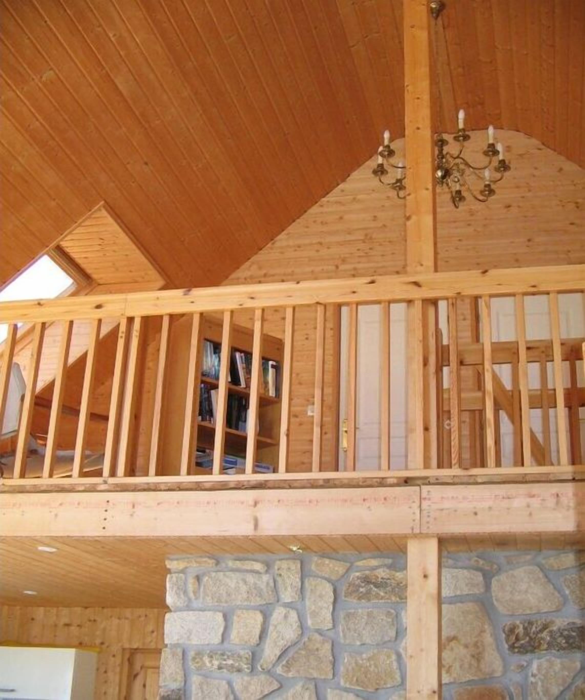 A wooden interior with a stone wall and a balcony with wooden railings.