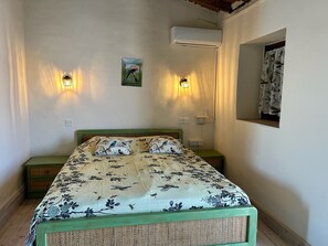 Un dormitorio con una cama, dos lámparas de pared, un equipo de aire acondicionado, un cuadro pequeño y un espejo.