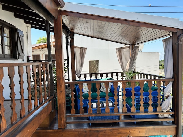 Un espace extérieur abrité, doté d’une rambarde en bois et de chaises rembourrées aux couleurs bleue et verte.