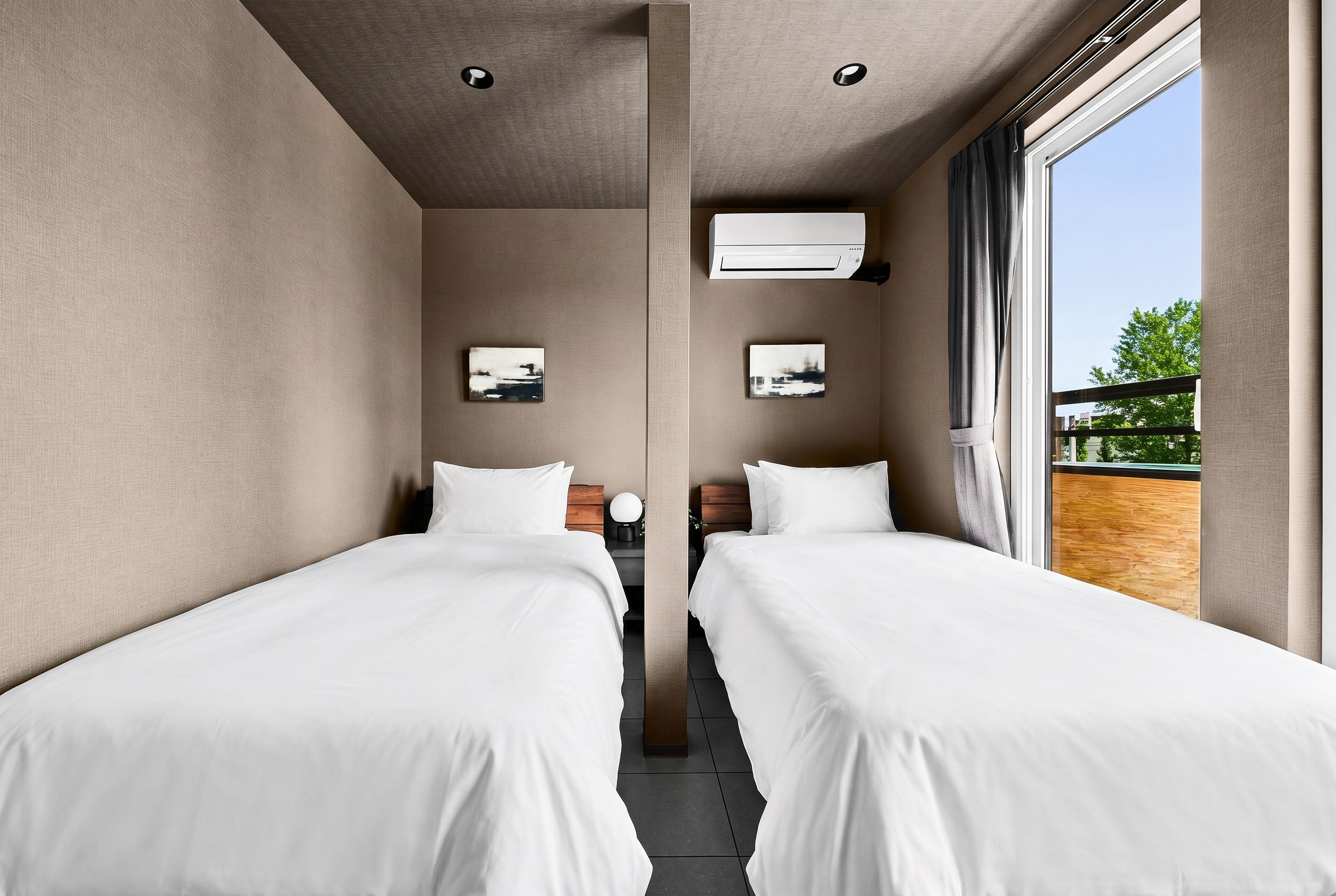 Een hotelkamer met twee eenpersoonsbedden, een groot raam, een airconditioning en kunstwerken aan de muur.