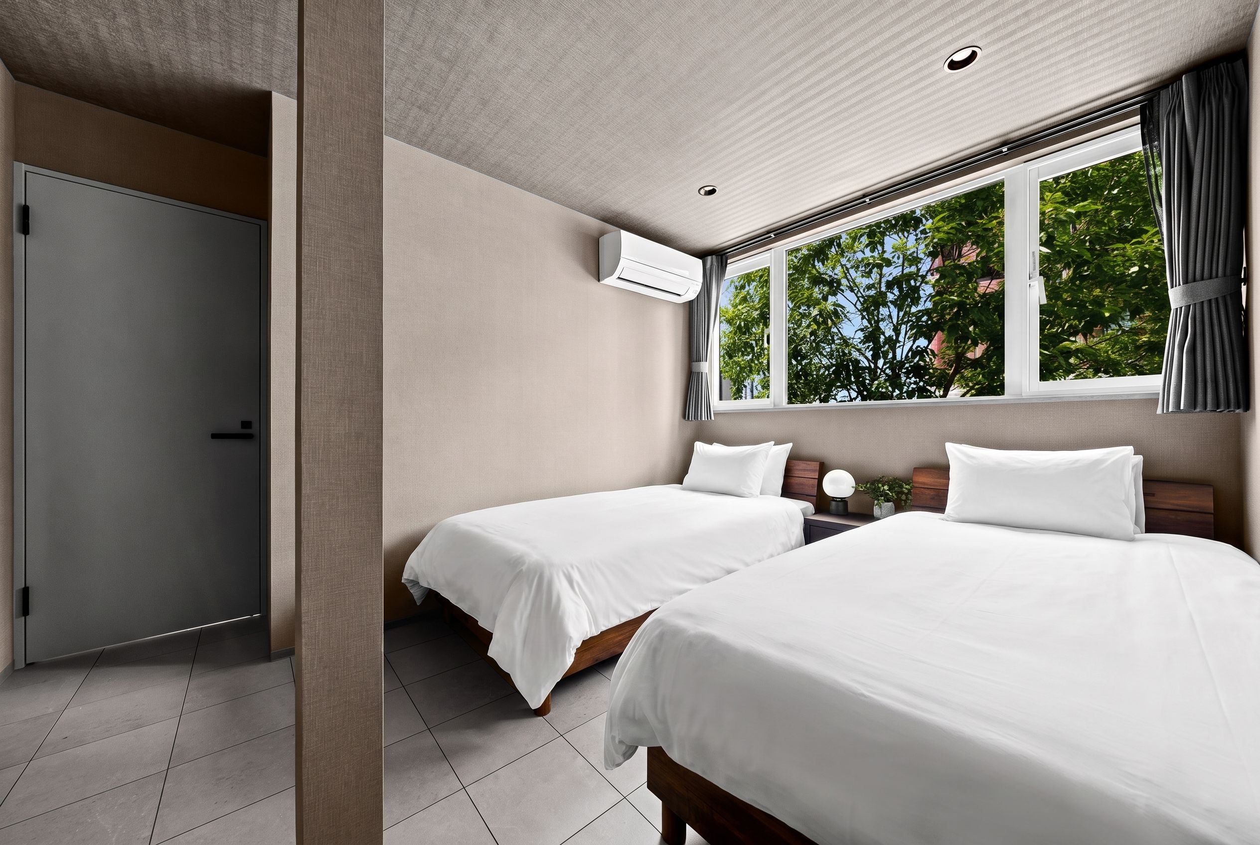 Quarto de hotel com duas camas, guarda-roupa e janela com vista para árvores.