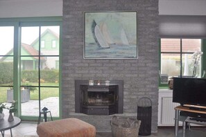 Een woonkamer met een open haard, een televisie en een schilderij van zeilboten.