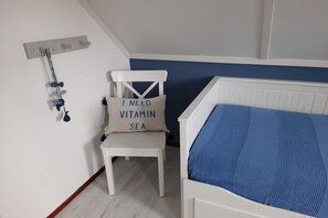 A bedroom with a bed, a chair, and a wall-mounted shelf. - Holiday home with 1 bedroom (Julianadorp aan Zee)