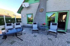 An outdoor patio with a table and chairs, a satellite dish, and a decorative sun emblem on the wall. - Holiday home with 1 bedroom (Julianadorp aan Zee)