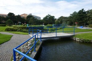 Een brug over een gracht met een blauwe reling, omgeven door groen en gebouwen.