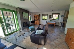 A spacious living area with a leather sofa, a dining table, and a kitchen in the background. - Holiday home with 1 bedroom (Julianadorp aan Zee)