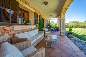 An outdoor patio with wicker furniture, a glass-top table, and a view of a green landscape. - House with pool Son San Marti Gran Muro (Muro)