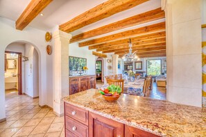 A spacious kitchen with a granite countertop, wooden cabinets, and a dining area with a chandelier. - House with pool Son San Marti Gran Muro (Muro)
