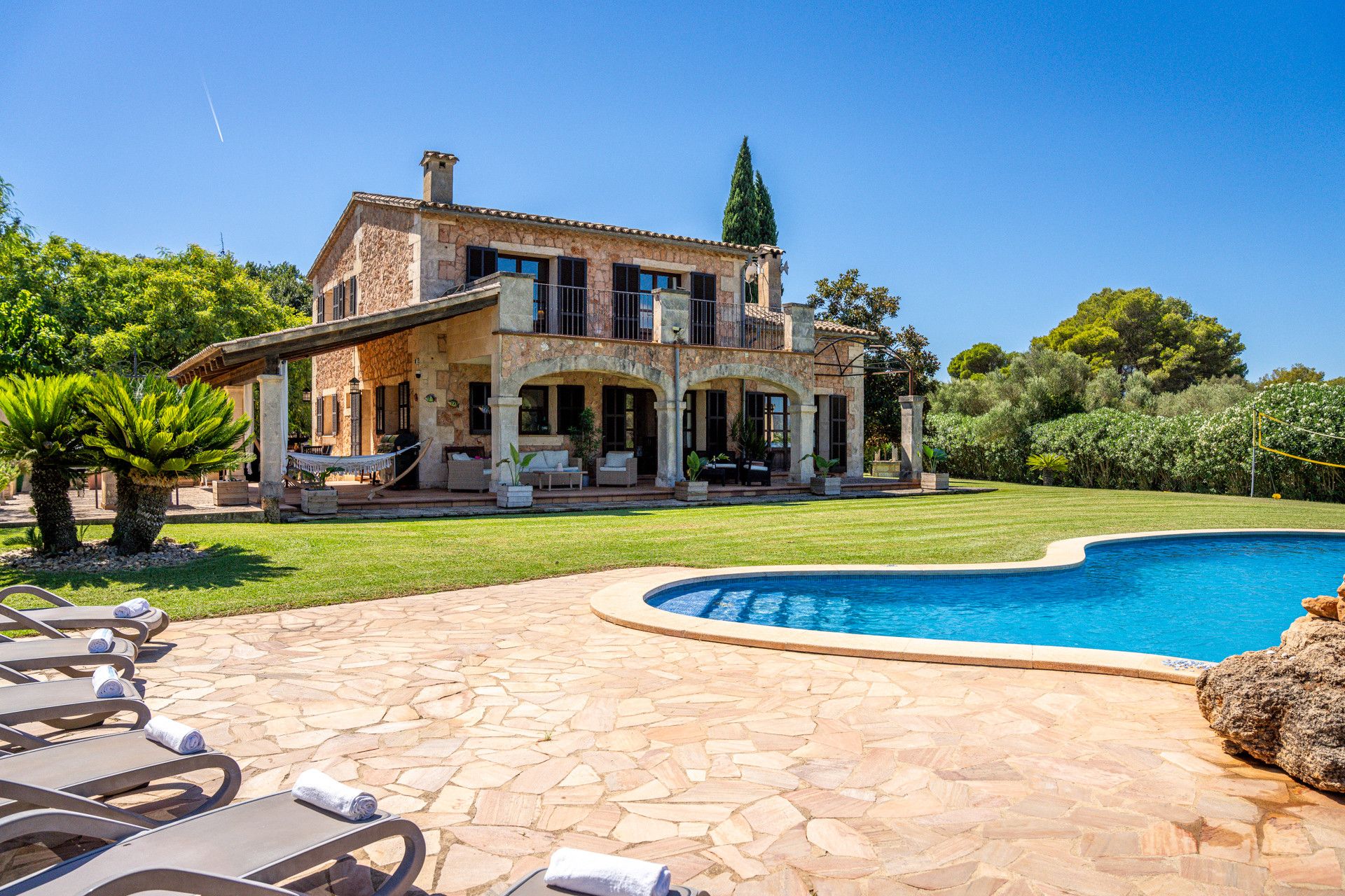 A two-story stone house with a swimming pool, outdoor seating, and a well-maintained lawn.
