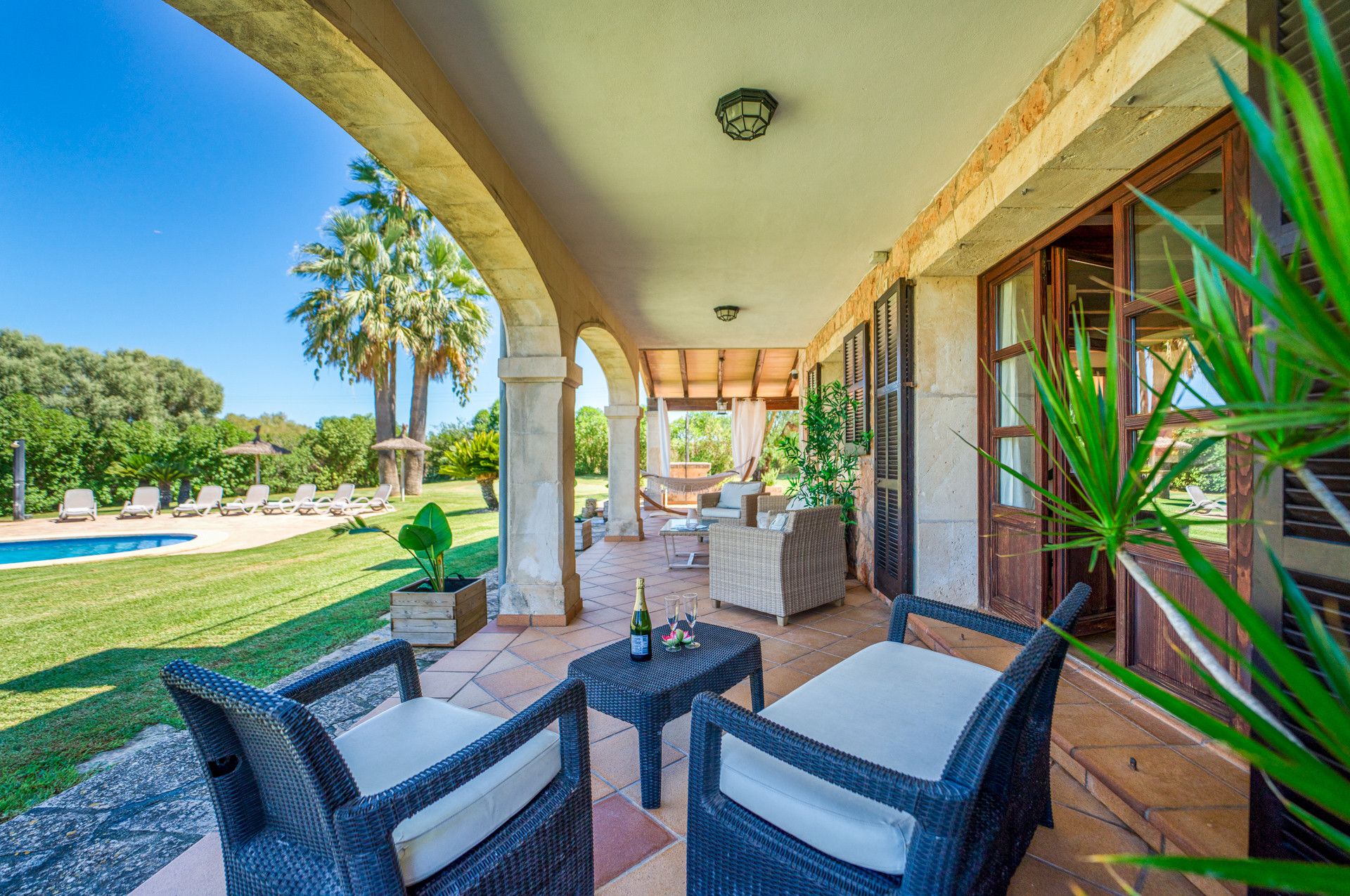 A covered outdoor patio with wicker furniture, a pool, and a view of the surrounding greenery.