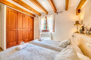 A bedroom with two beds, wooden beams on the ceiling, a large wooden wardrobe, a window with curtains, and a bedside lamp. - House with pool Son San Marti Gran Muro (Muro)