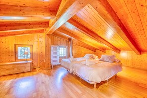 Quarto de cabana de madeira com teto alto, cama, janela e estante embutida.