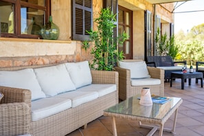 Un espace extérieur aménagé avec des meubles en osier, une table en verre et des plantes en pot.