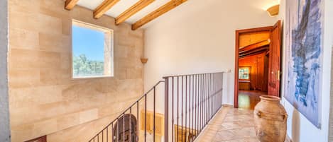 A staircase with a wooden ceiling and stone walls, leading to a room with a window and a door.