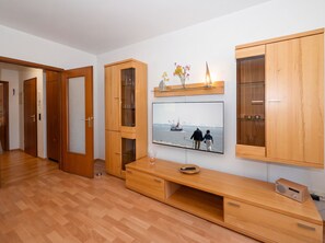 A modern living room with wooden cabinets, a glass coffee table, and a flat-screen TV mounted on the wall. - Stunning Vacation Rental No. 32 at Haus Schloss am Meer in a Central Location (Büsum)