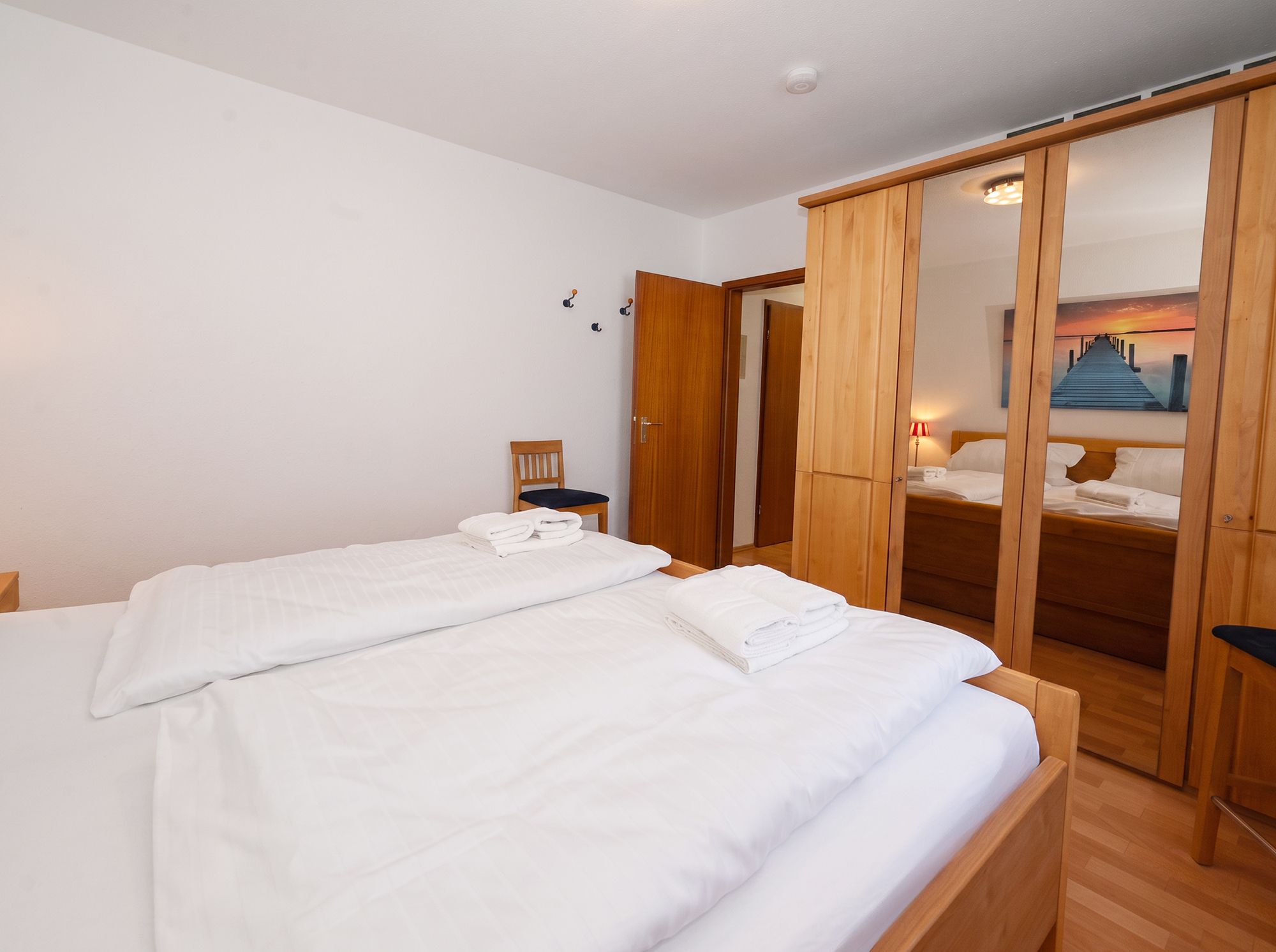 A bedroom with two beds, wooden wardrobe, and a view of a pier through a mirror.